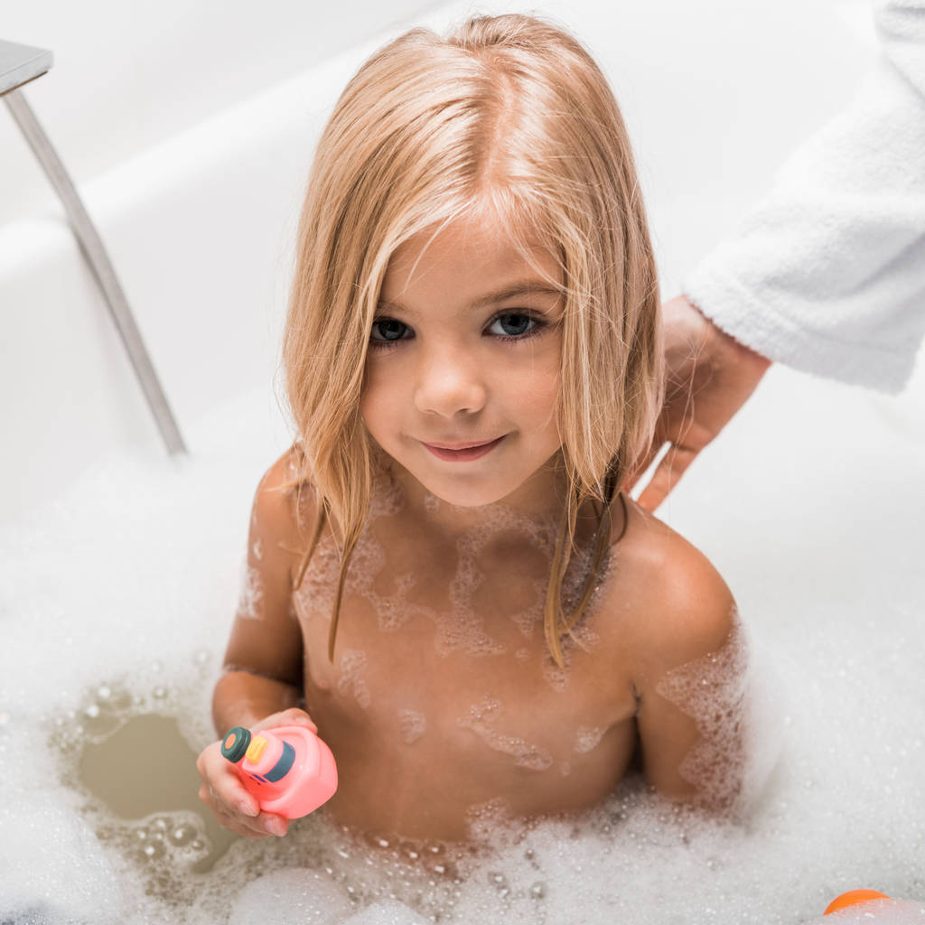 Güzel bir çocuğun banyo yapmasını ve annesinin yanında lastik oyuncaklar tutmasını.  - Fotoğraf, Görsel