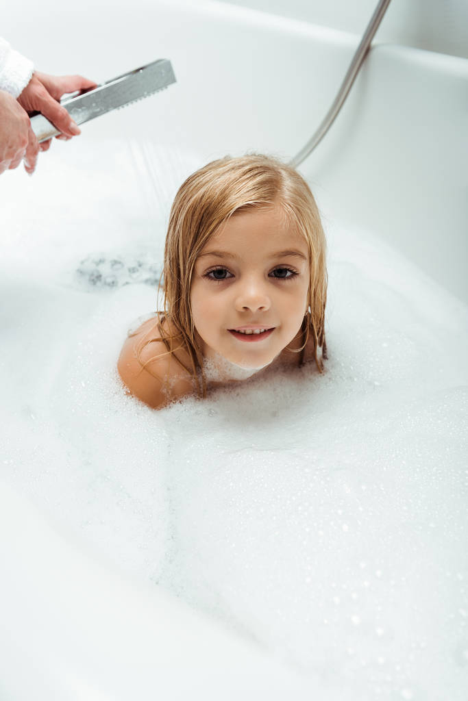 очаровательный и голый ребенок принимает ванну рядом с матерью в ванной комнате
  - Фото, изображение