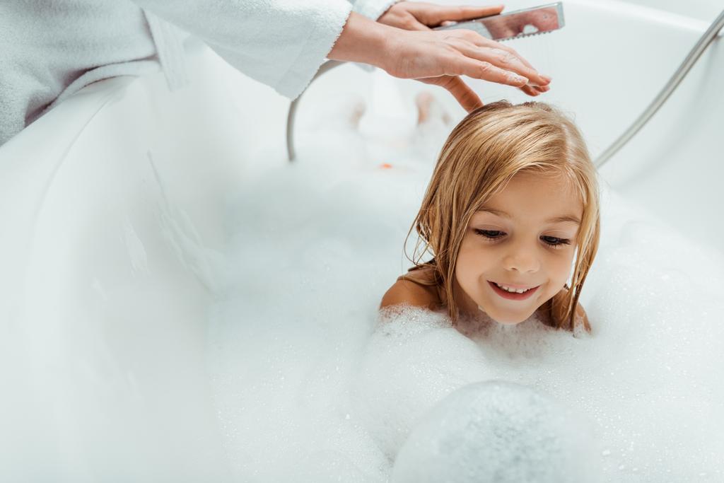 entzückendes und nacktes Kind badet in der Nähe der Mutter im Badezimmer  - Foto, Bild