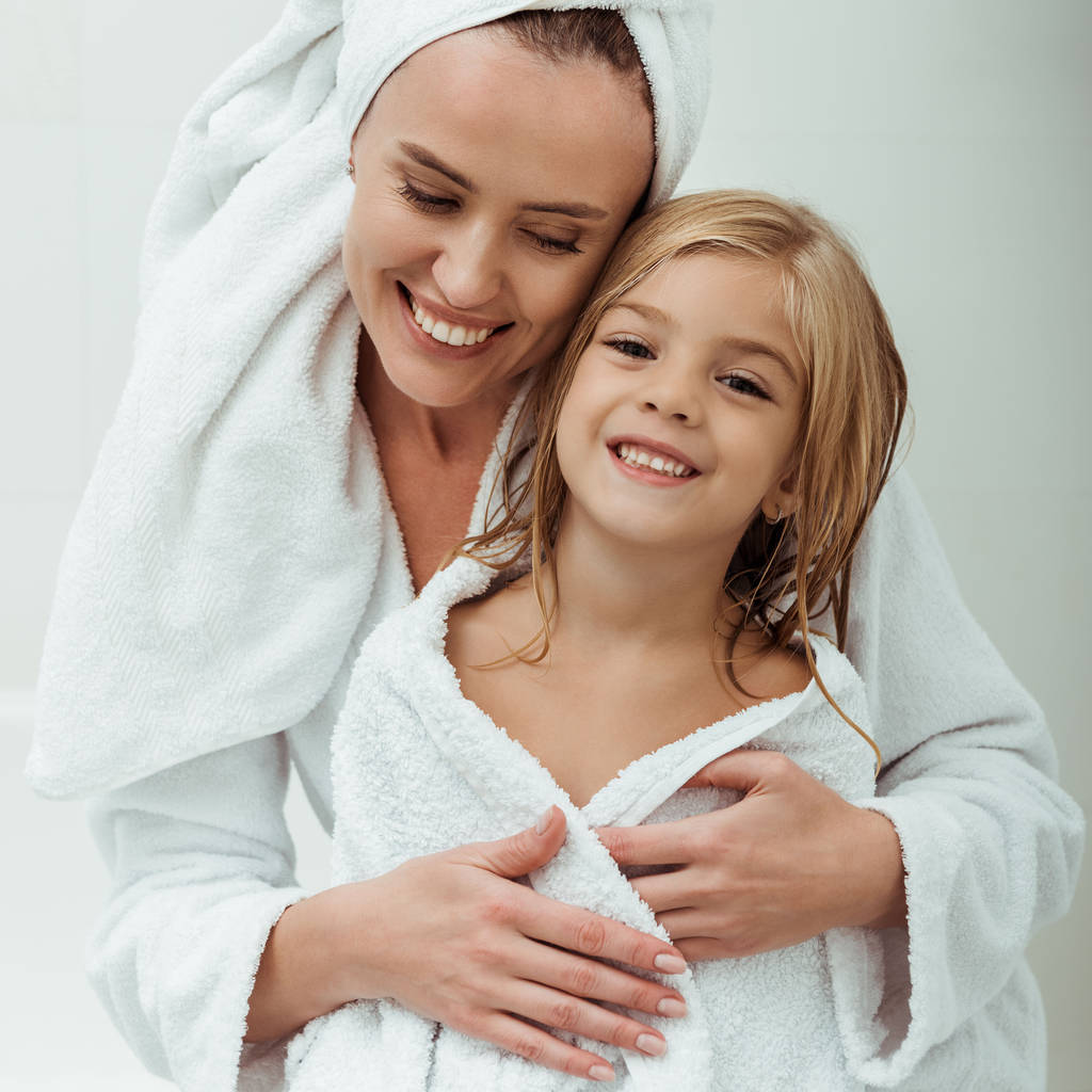 Χαρούμενη μητέρα χαμογελώντας αγκαλιάζοντας την κόρη στο μπάνιο  - Φωτογραφία, εικόνα