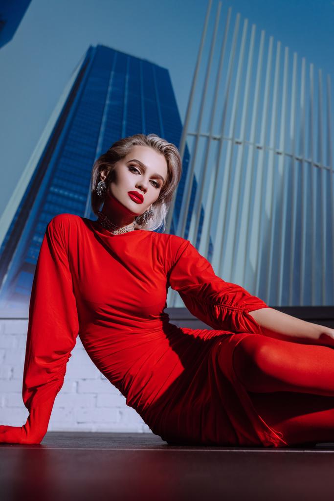 Şehrin arka planında oturan kırmızı elbiseli çekici ve şık bir kadın.  - Fotoğraf, Görsel