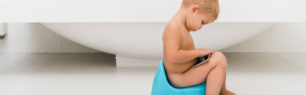 panoráma lövés kisgyerek ül a kék bili és gazdaság okostelefon közelében fürdőkád  - Fotó, kép