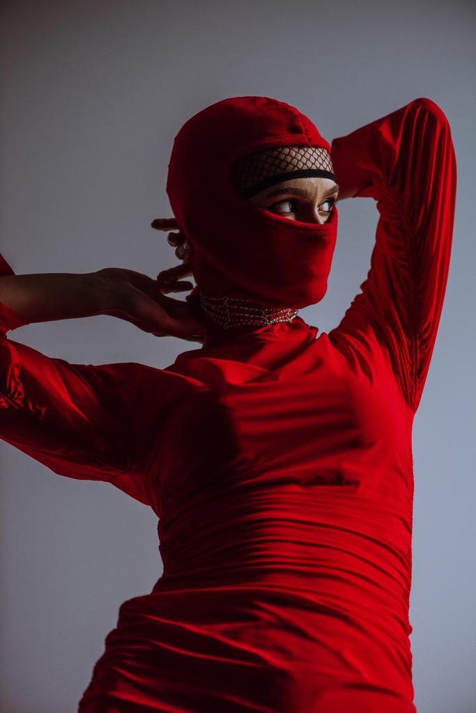 stylish woman in red dress and balaclava isolated on grey - Photo, Image