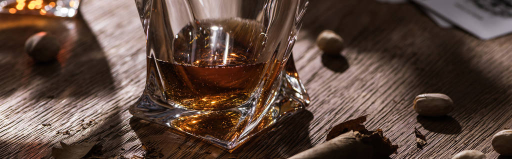 Glas cognac met sigaar en pistachenoten op houten tafel, panoramisch schot - Foto, afbeelding