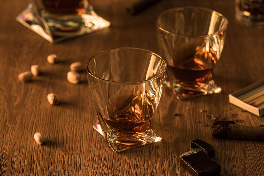 Sklenice brandy s pistáciemi, doutníkem a zapalovačem na dřevěném stole - Fotografie, Obrázek