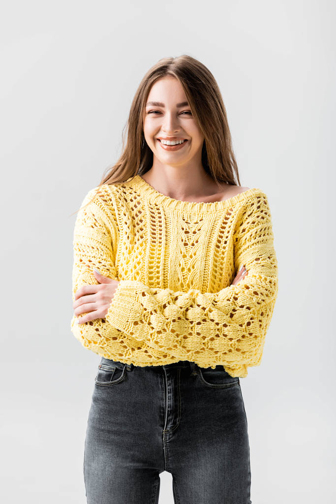 alegre chica en suéter amarillo de pie con brazos cruzados aislados en gris
 - Foto, Imagen