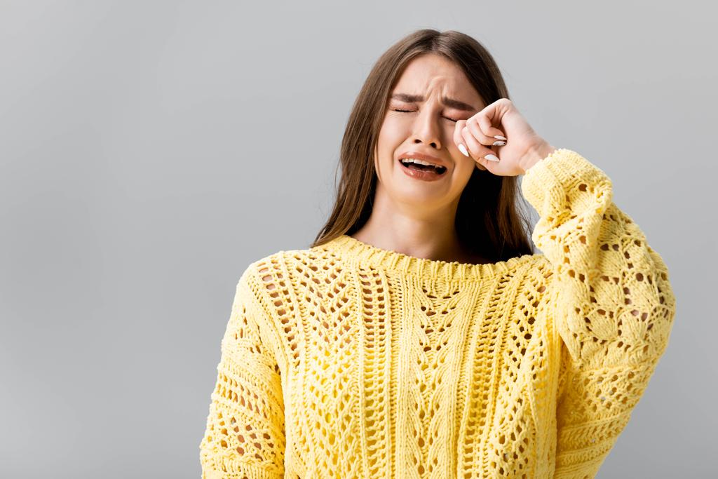 προσβεβλημένο κορίτσι με κίτρινο πουλόβερ κλαίει και σκουπίζει δάκρυα με το χέρι απομονώνονται σε γκρι - Φωτογραφία, εικόνα