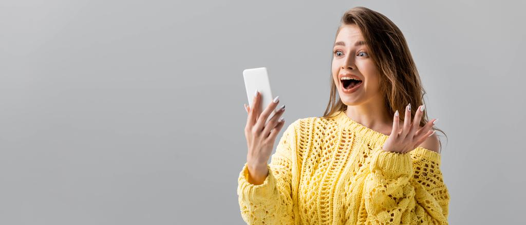 plano panorámico de chica impactada mostrando wow gesto durante el chat de vídeo en el teléfono inteligente aislado en gris
 - Foto, imagen