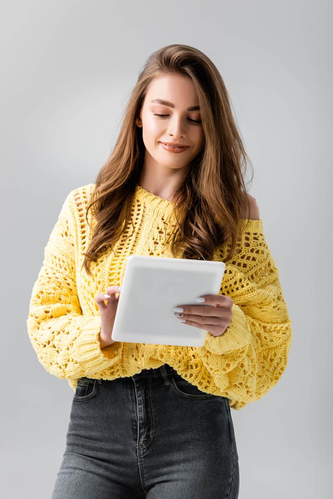 mosolygós lány sárga pulóver segítségével digitális tabletta elszigetelt szürke - Fotó, kép