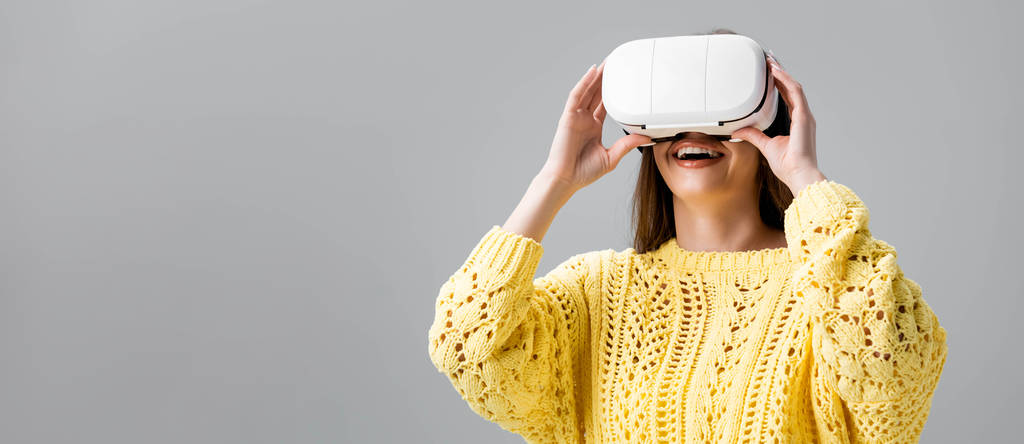панорамный снимок веселой девушки с помощью гарнитуры виртуальной реальности, изолированной на сером
 - Фото, изображение