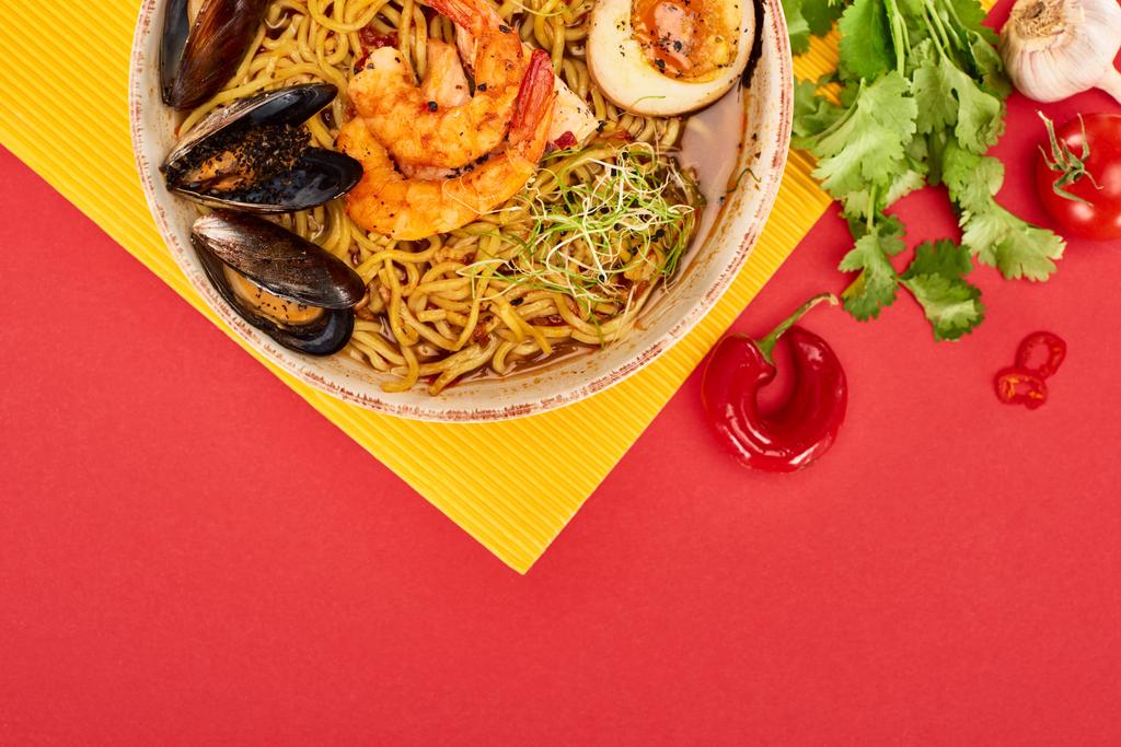 黄色と赤の表面に新鮮な食材の近くの辛い魚介ラーメンのトップビュー - 写真・画像