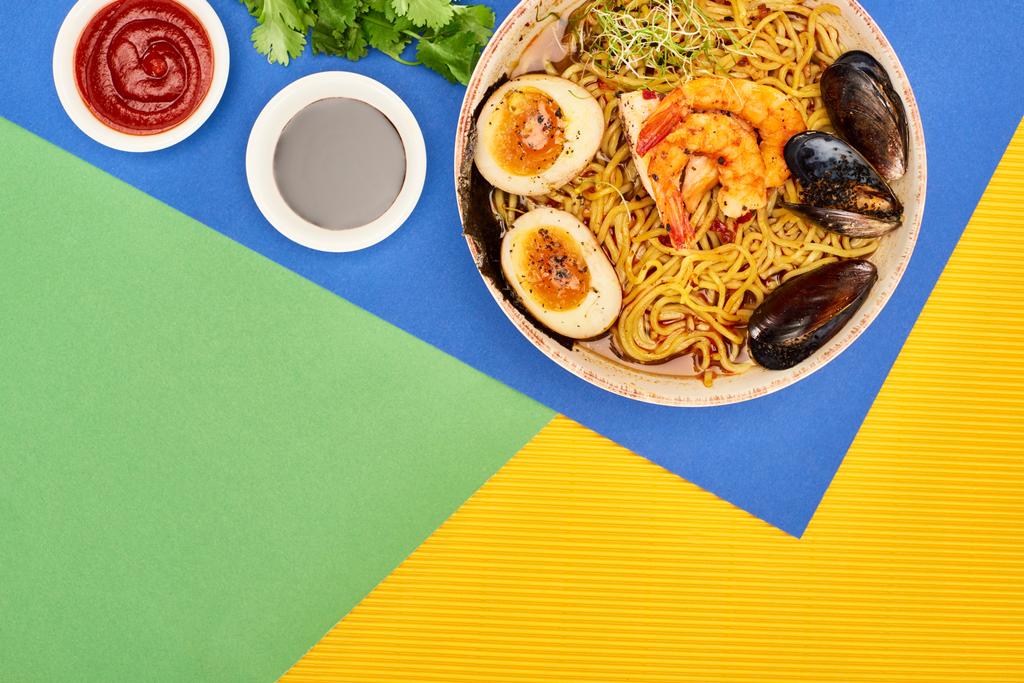 vue de dessus des ramen épicés de fruits de mer près des sauces chili et soja sur la surface multicolore
 - Photo, image
