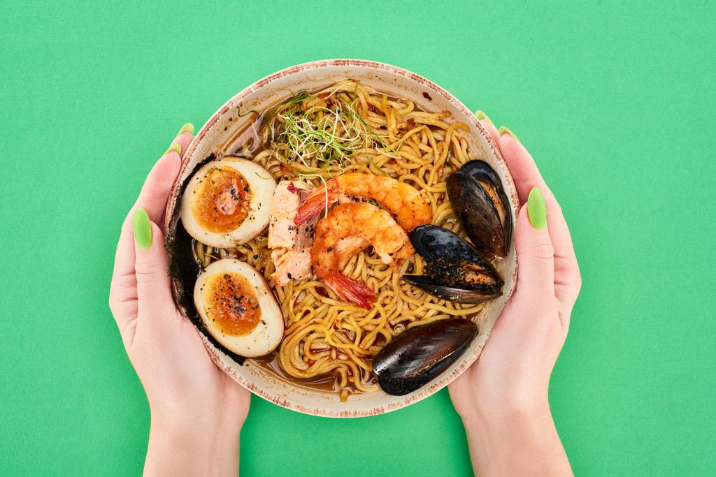 cropped view of woman holding bowl with spicy seafood ramen on green surface - Photo, Image