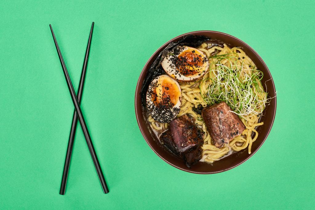 κορυφαία άποψη του πικάντικου ράμεν κρέατος κοντά chopsticks απομονώνονται σε πράσινο - Φωτογραφία, εικόνα