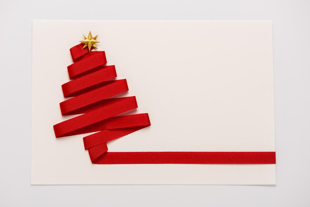 Draufsicht auf rotes Band mit goldener sternförmiger Schleife auf Papierumschlag isoliert auf weiß  - Foto, Bild