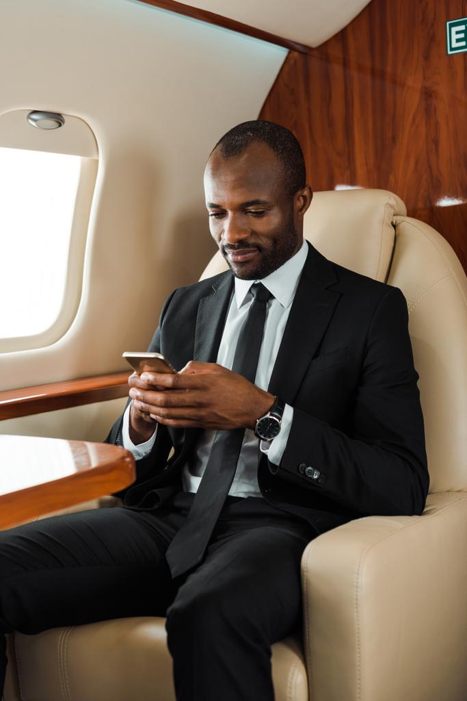komea afrikkalainen amerikkalainen liikemies puku käyttäen älypuhelin yksityinen suihkukone
  - Valokuva, kuva