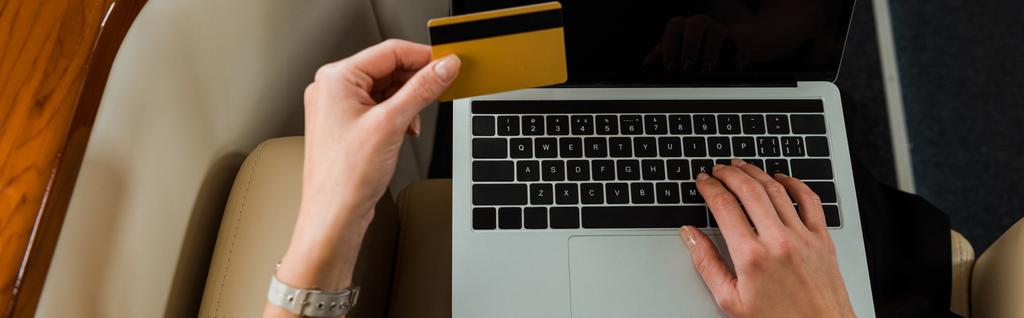 panoramisch schot van zakenvrouw met creditcard in de buurt van laptop in prive-jet  - Foto, afbeelding