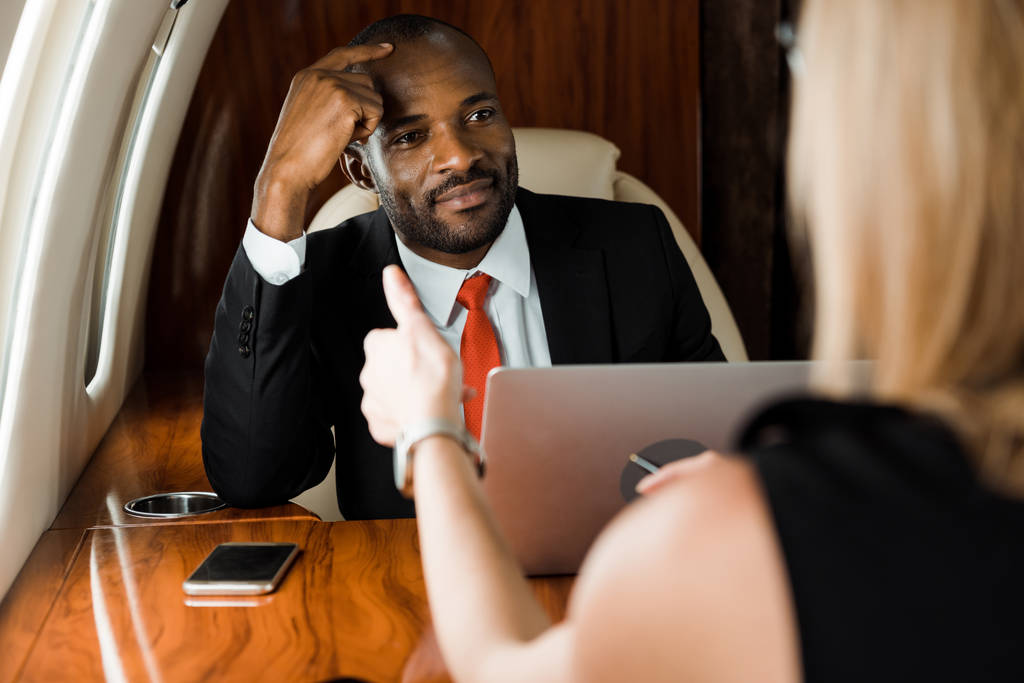 избирательный фокус африканского американского бизнесмена, смотрящего на деловую женщину в частном самолете
  - Фото, изображение