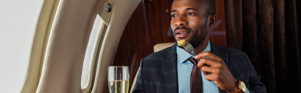 plano panorámico del hombre afroamericano comiendo en jet privado
  - Foto, Imagen