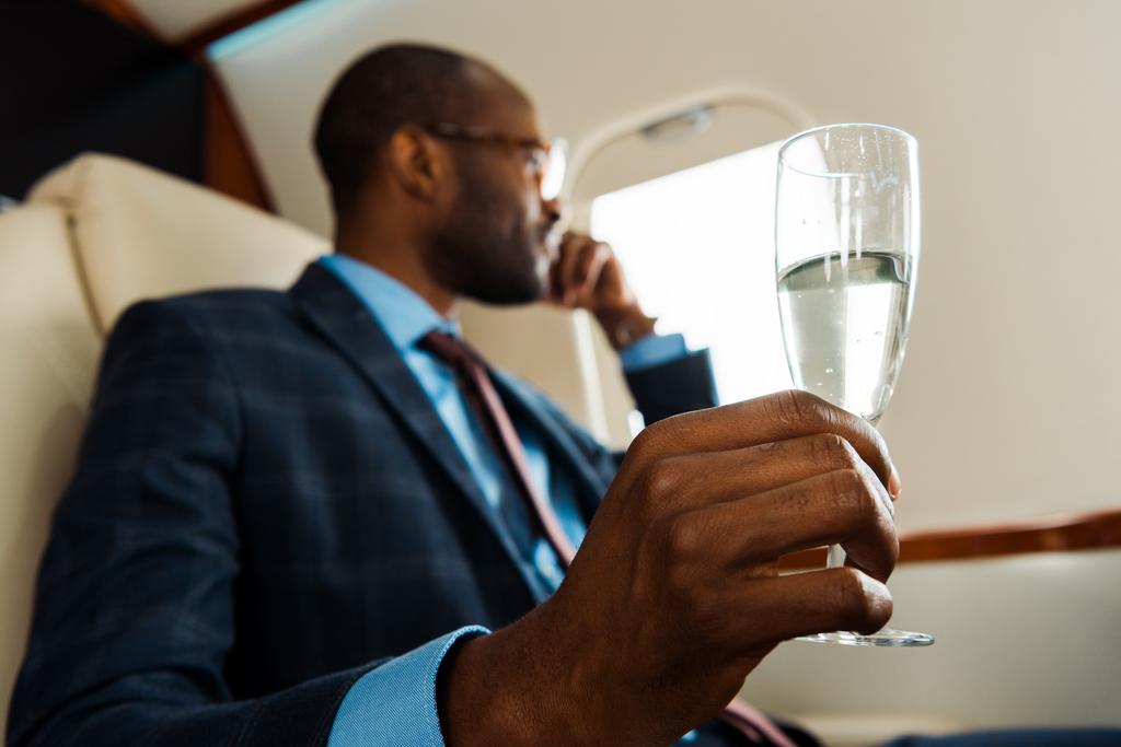 selectieve focus van Afro-Amerikaanse man met champagne glas in prive-vliegtuig  - Foto, afbeelding