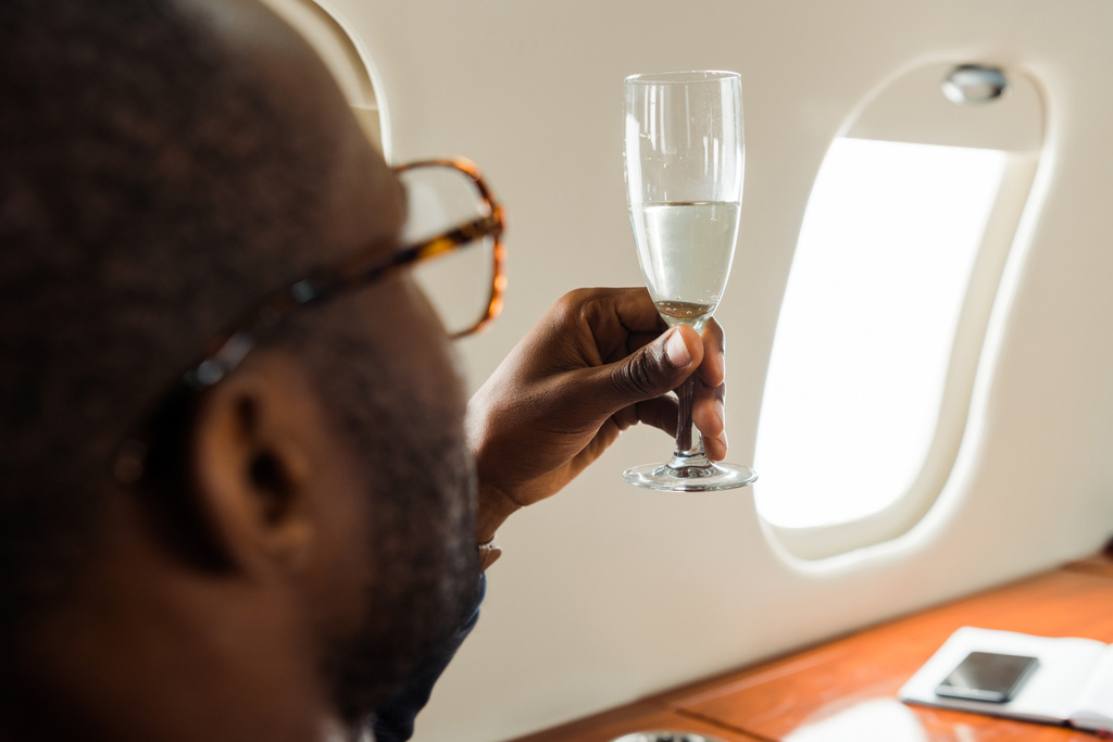 selective focus of african american businessman in glasses holding champagne in private jet  - Photo, Image