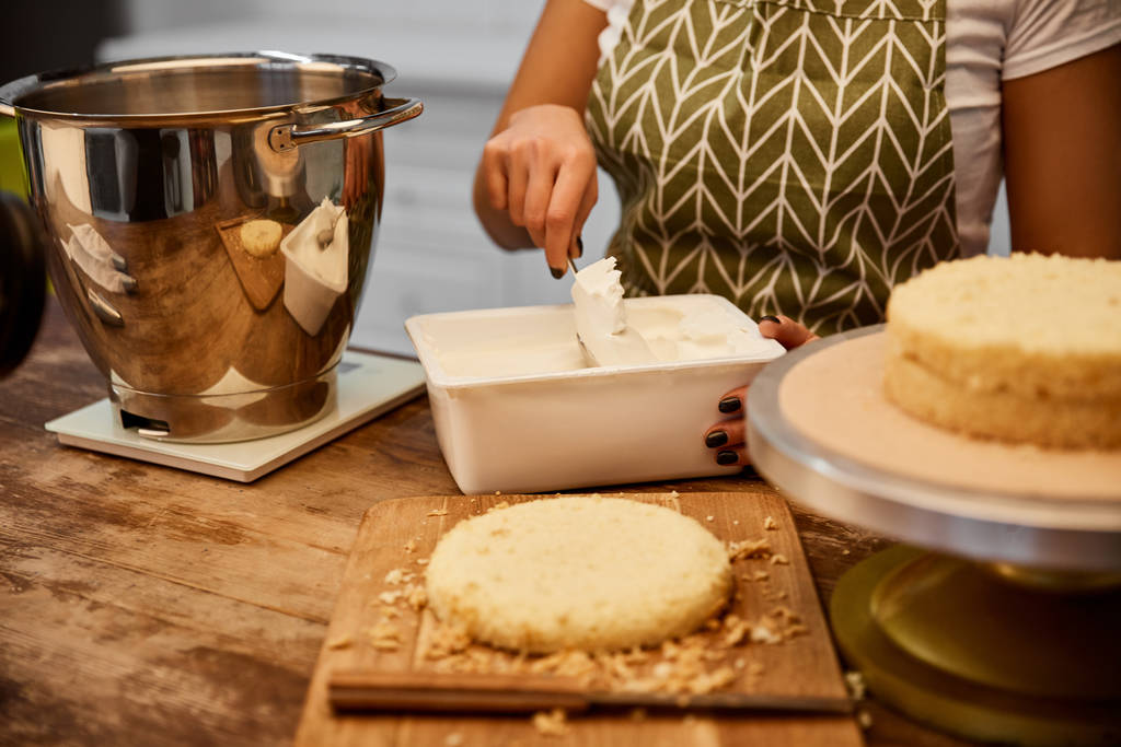 Επιλεκτική εστίαση του ζαχαροπλάστη λαμβάνοντας κρέμα για το μαγείρεμα κέικ στην κουζίνα  - Φωτογραφία, εικόνα