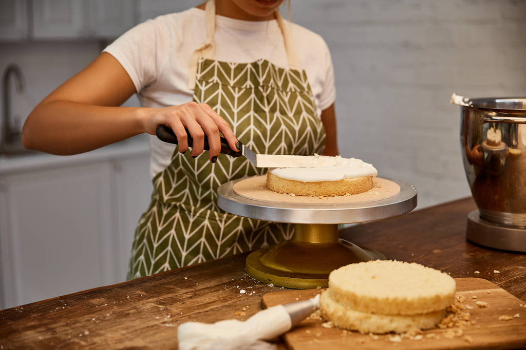 Cropped view of confectioner putting cream with spatula on cake layer - 写真・画像