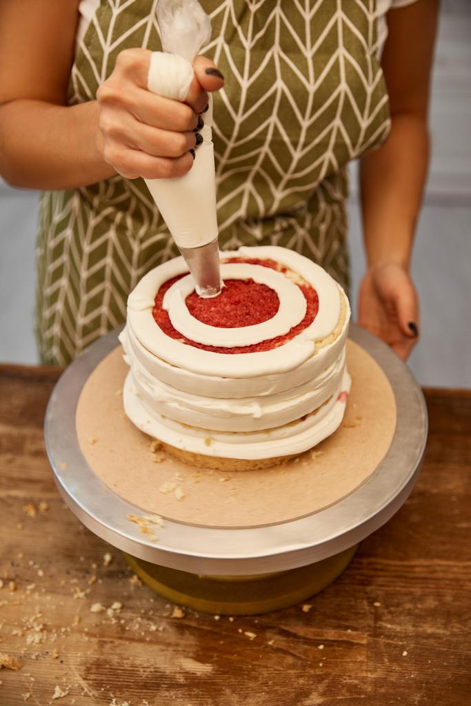Vista recortada del pastelero agregando crema de la bolsa de pastelería en la torta
  - Foto, Imagen