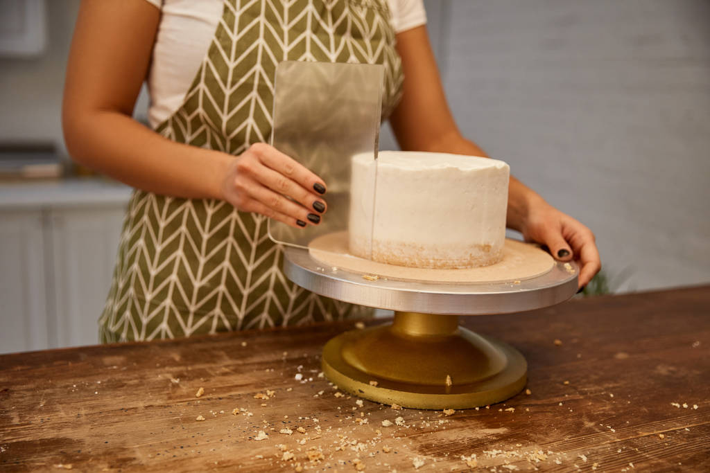 Şeffaf kazıyıcı ve pastada lezzetli kremayla çalışan şekerlemecinin kırpılmış görüntüsü  - Fotoğraf, Görsel