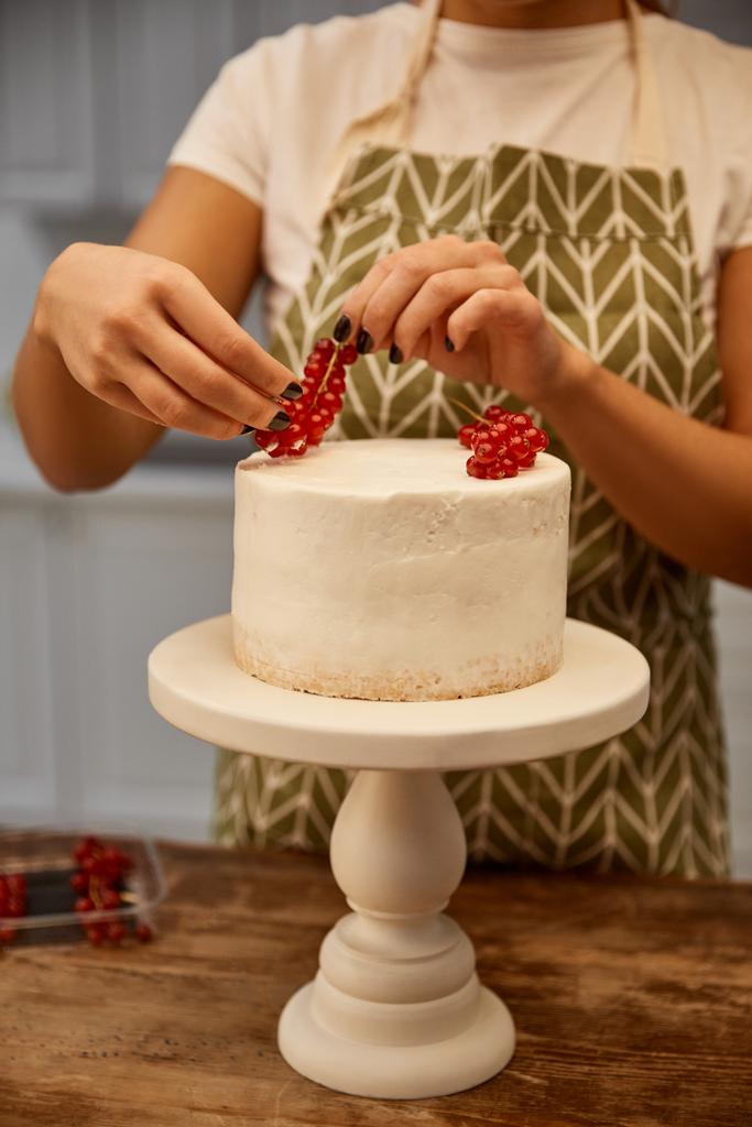 Vista recortada del confitero añadiendo grosella roja en la torta
 - Foto, Imagen