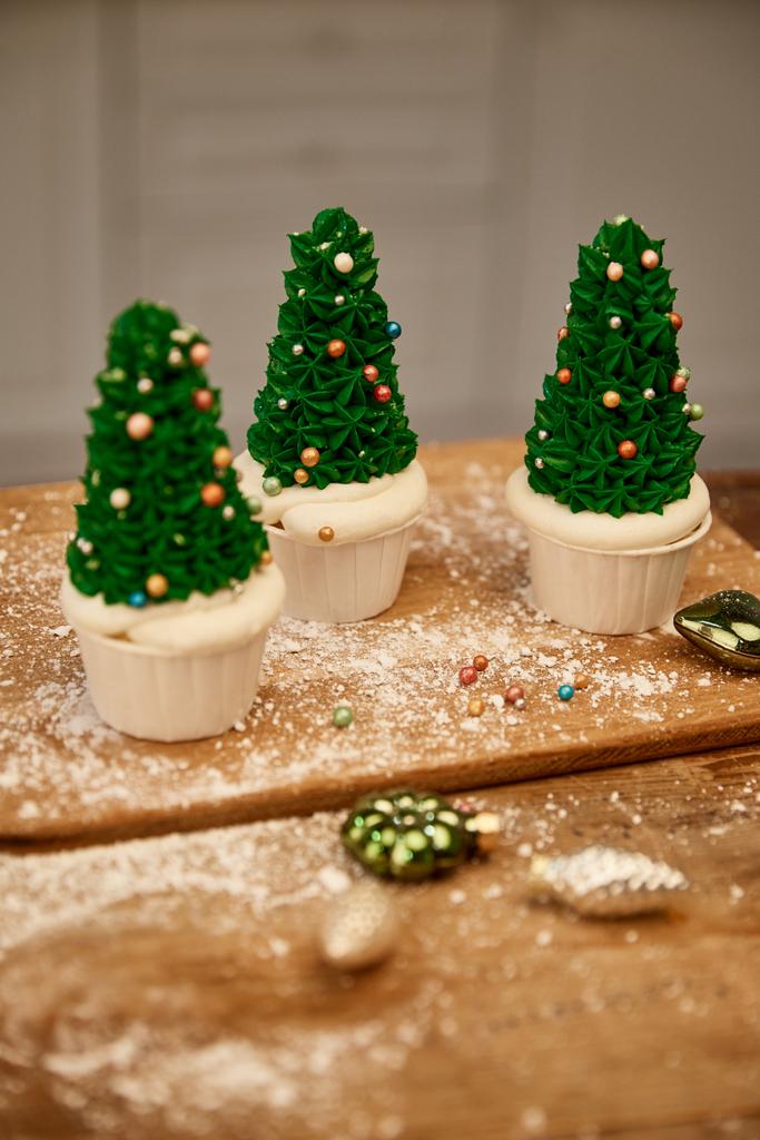 Tasty Christmas tree cupcakes with green cream and decorations on cutting board with christmas balls - Photo, Image