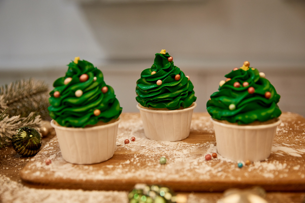 Прикрашені кекси з зеленим кремом і різдвяними кульками з ялиновим гілкою на столі
 - Фото, зображення