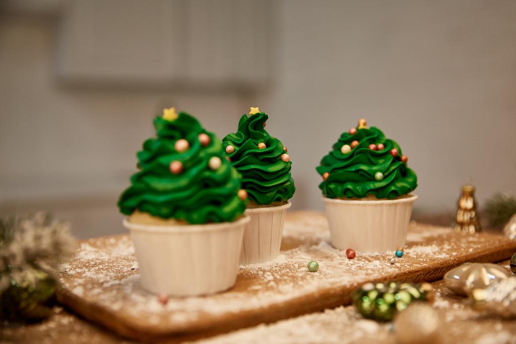 Selective focus of sweet cupcakes with christmas balls and spruce branch on cutting board - Photo, Image