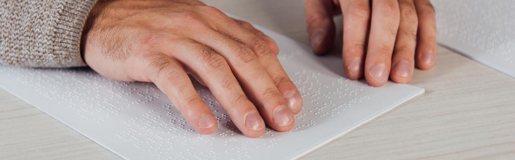 Oříznutý pohled na vázaného muže, jak čte Braillovo písmo na papíře u stolu, panoramatický záběr - Fotografie, Obrázek