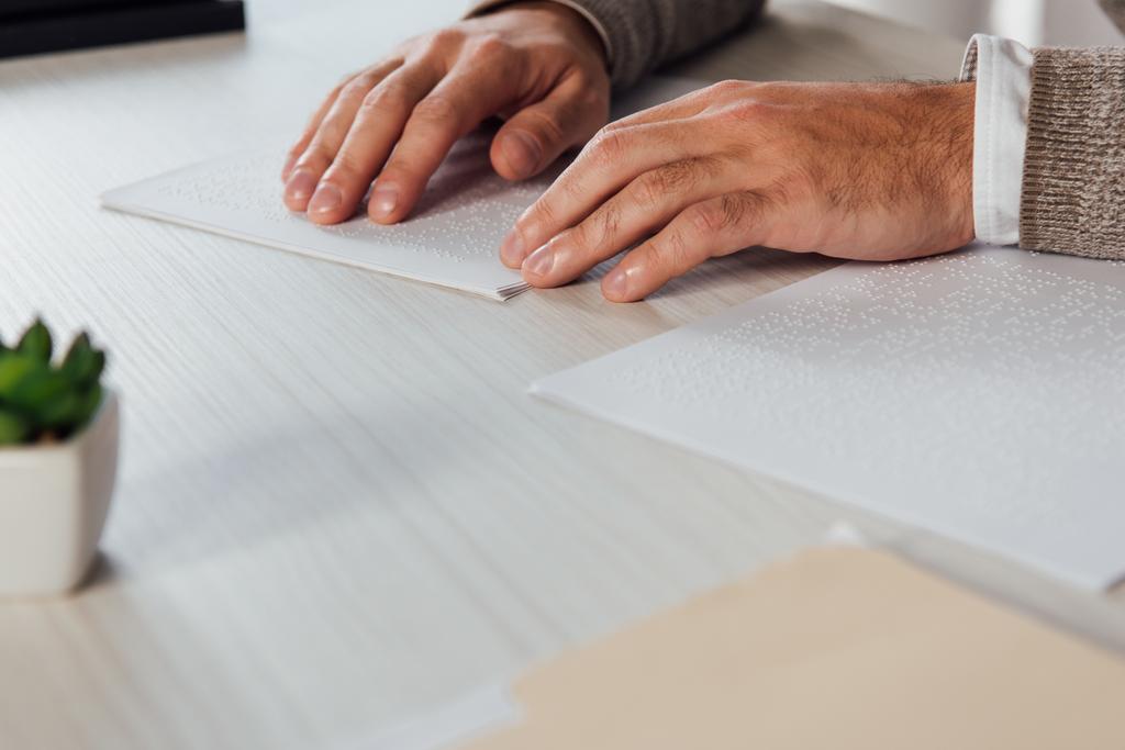 Gewassen weergave van blinde man die braille lettertype leest van papier aan tafel - Foto, afbeelding