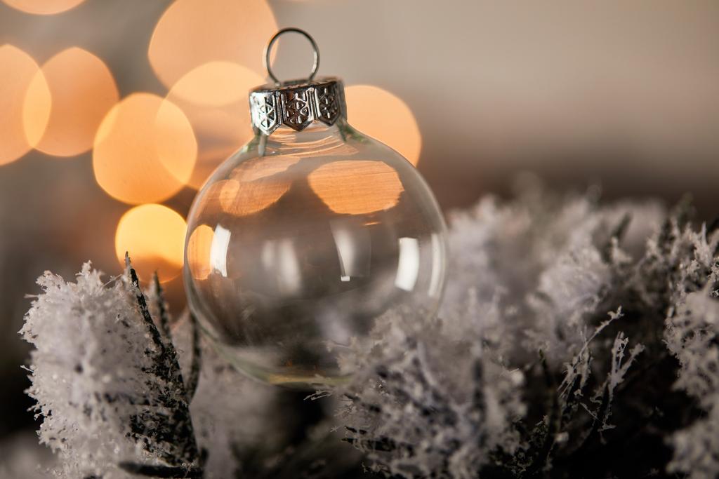 decoratieve transparante kerstbal op sparren takken in de sneeuw met wazig geel licht - Foto, afbeelding