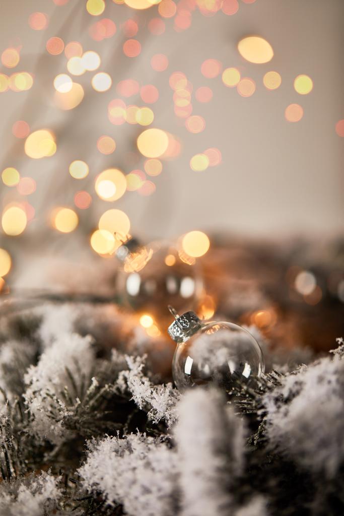 transparent christmas balls on spruce branches in snow with blurred yellow lights - Photo, Image