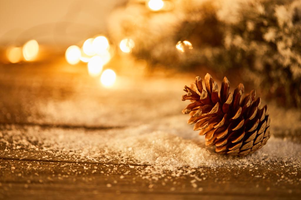 cône de pin décoratif sur table en bois avec branches d'épinette dans la neige et lumières de Noël bokeh
 - Photo, image