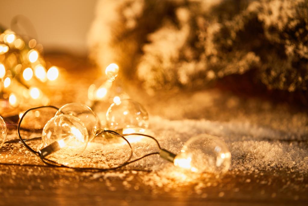 Різдвяна гірлянда з прозорими лампочками на дерев'яній поверхні з ялиновими гілками в снігу
  - Фото, зображення