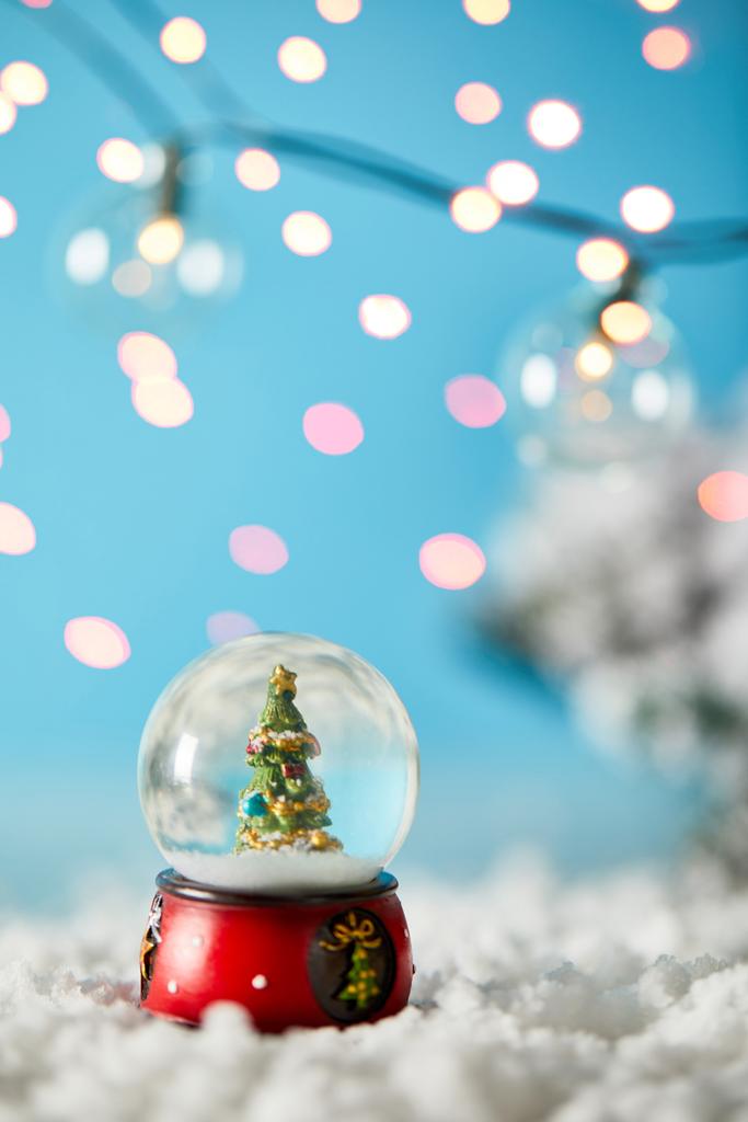 sapin de Noël en boule de neige debout sur bleu avec neige et lumières floues
 - Photo, image