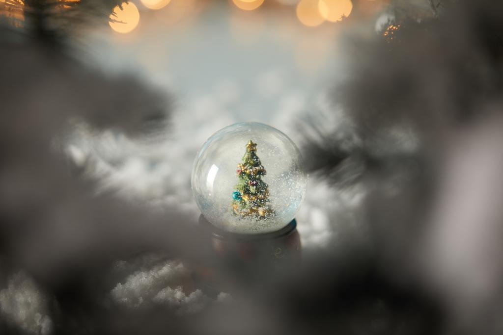 selektywne skupienie małej kuli śnieżnej z choinką stojącą w śniegu z gałązkami świerku i światłami bokeh  - Zdjęcie, obraz