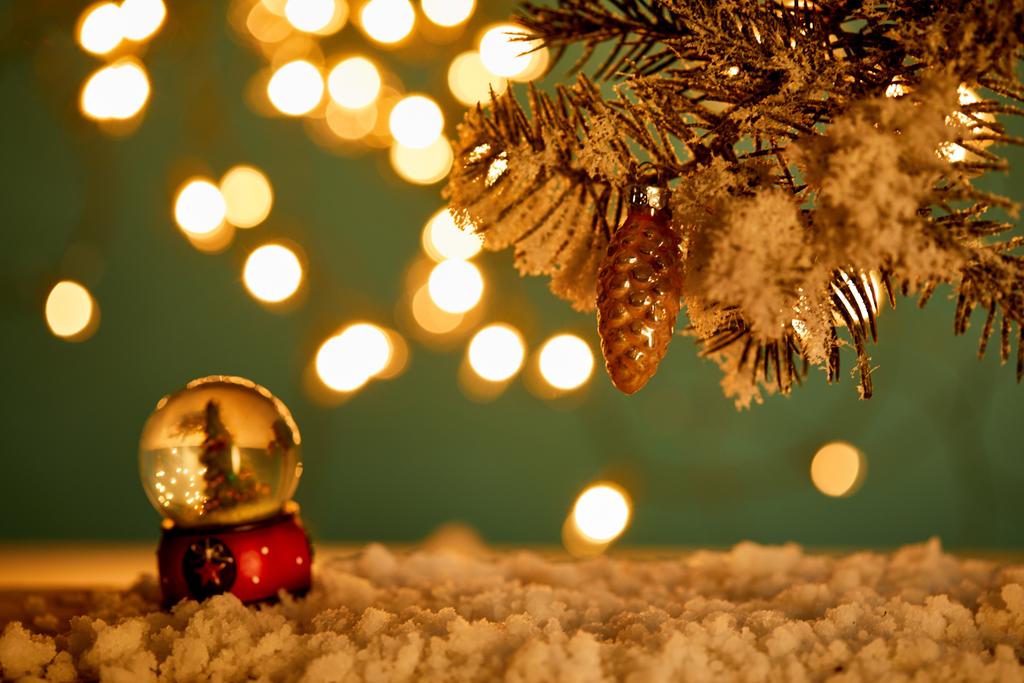 снежок с рождественской ёлкой, стоящей в снегу с еловыми ветвями, рождественским мячом и размытыми огнями ночью
  - Фото, изображение