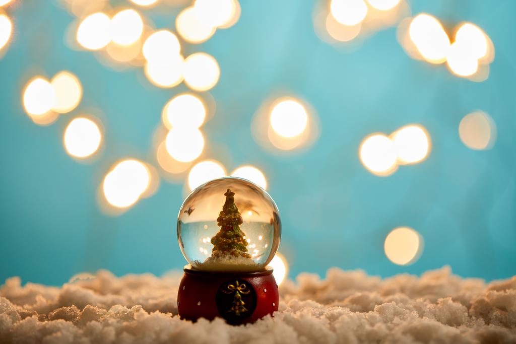 mała choinka w śnieżnej kuli stojącej na niebiesko ze śniegiem i rozmazanymi światłami  - Zdjęcie, obraz