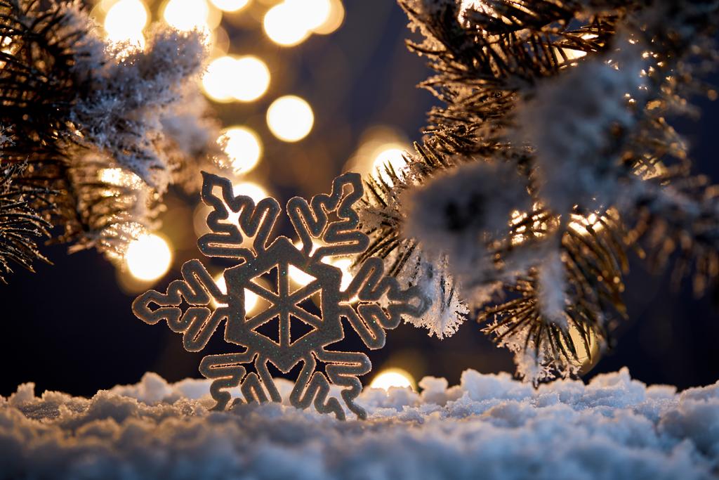 zblízka dekorativní sněhové vločky se smrkovými větvemi ve sněhu s rozmazanými vánočními světly  - Fotografie, Obrázek