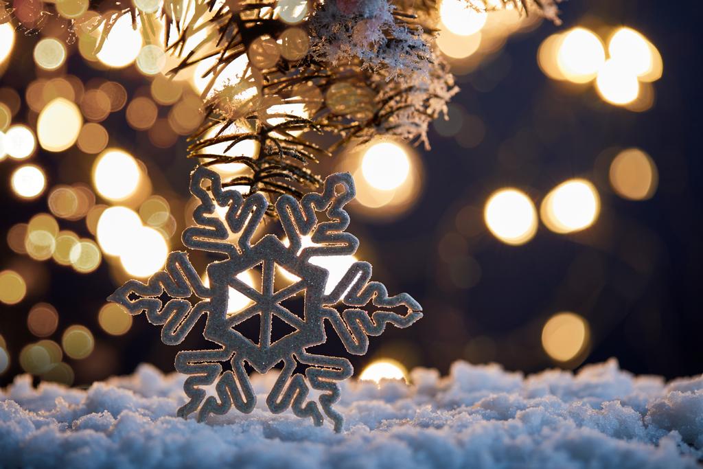 decoratieve sneeuwvlok met sparren takken in de sneeuw met kerstverlichting bokeh  - Foto, afbeelding