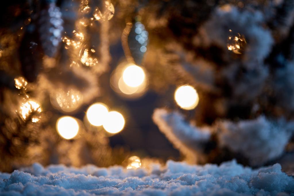close-up van sparren takken in de sneeuw met kerst ballen en lichten bokeh 's nachts   - Foto, afbeelding