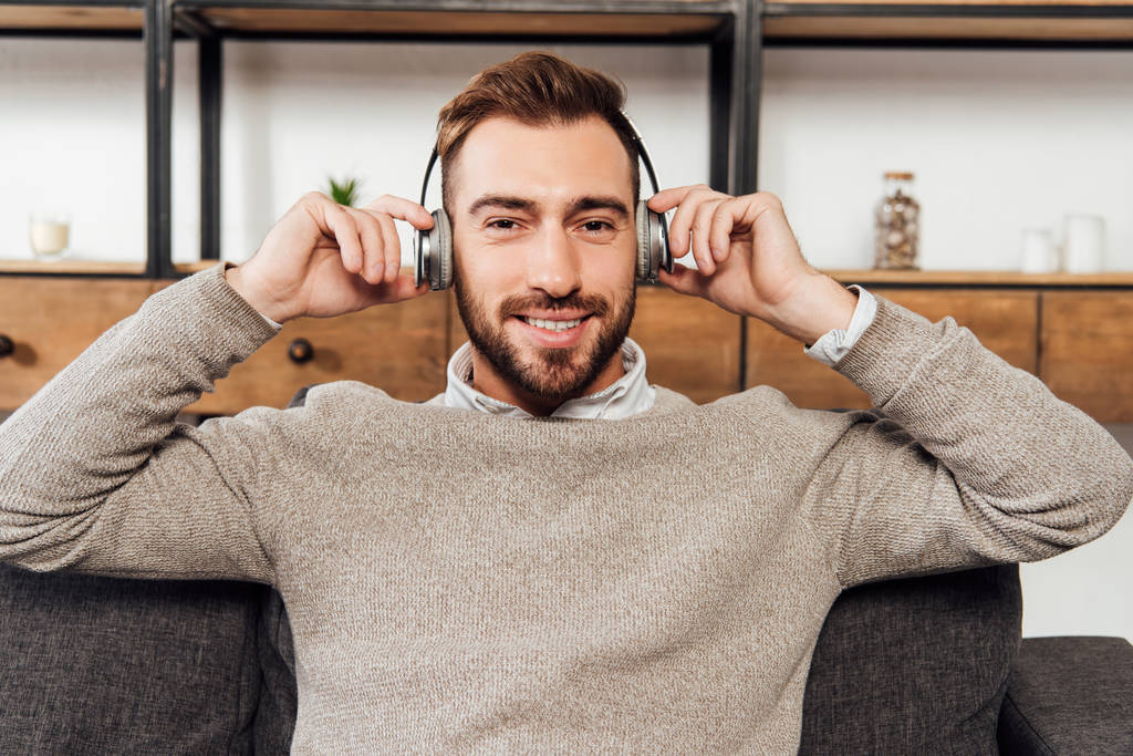 Smiling man in headphones sitting on sofa in living room - Photo, Image