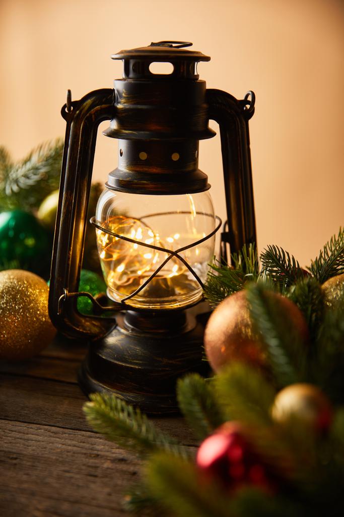 декоративная винтажная масляная лампа с огнями, еловыми ветвями и рождественскими шарами на бежевом
 - Фото, изображение
