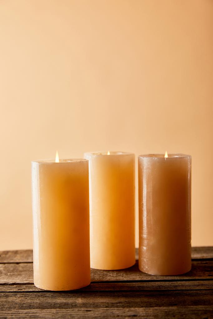 három ünnepi égő gyertya fából készült asztalon bézsen  - Fotó, kép