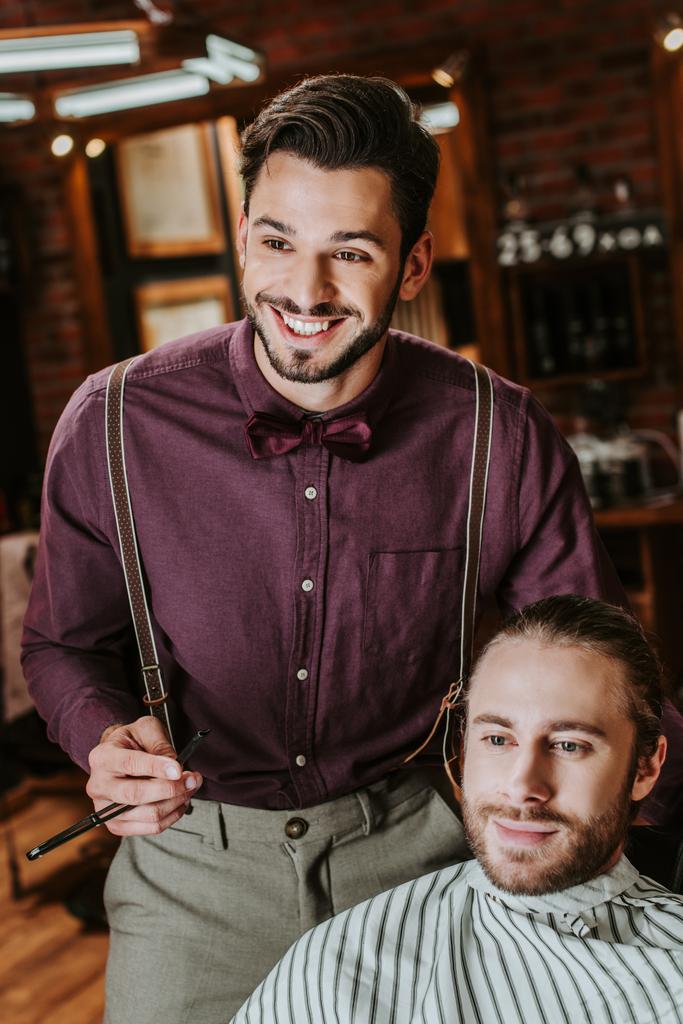 床屋で髭の男の近くに剃刀を持っている陽気な理髪店  - 写真・画像